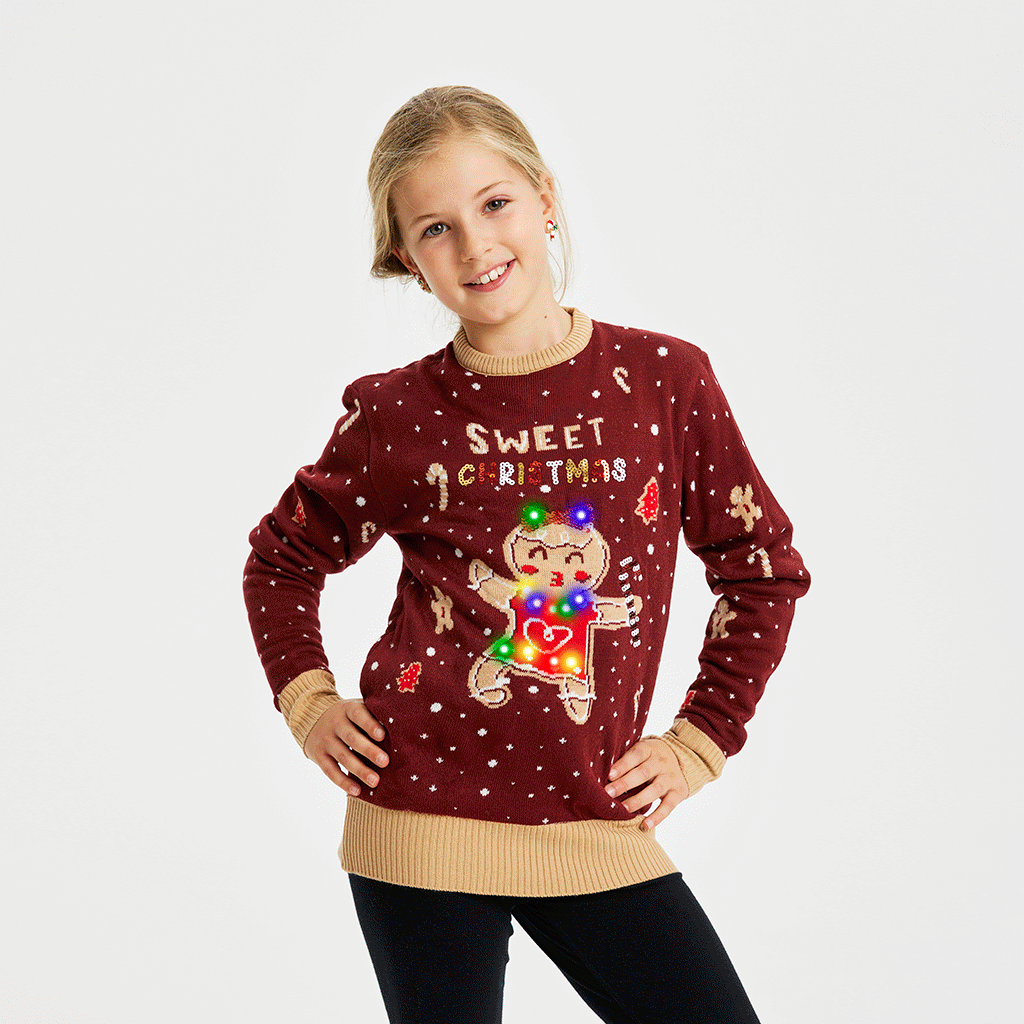 Et smilende barn iført en julesweater i rød med en kagekone, der danser og lyser.